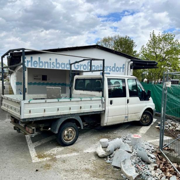 Ein weißer Transporter steht vor einem Gebäude mit der Aufschrift „Erlebnisbad Großpetersdorf“, daneben liegen Bauschutt und Steine.