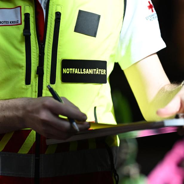 Eine Person in einer gelben Notfallsanitäter-Weste schreibt mit einem Stift auf ein Klemmbrett.