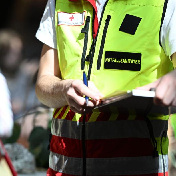 Ein Notfallsanitäter mit gelber Weste schreibt mit einem Stift auf ein Klemmbrett.