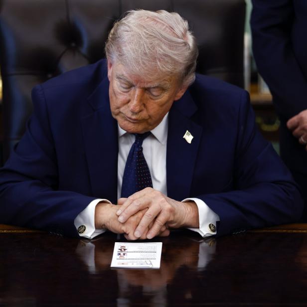 Donald Trump sitzt am Schreibtisch und betrachtet ein Dokument.