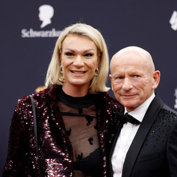 Maria Riesch mit blondem Haar und Johann Schrempf im Anzug posieren gemeinsam vor einem dunklen Hintergrund mit Logos.