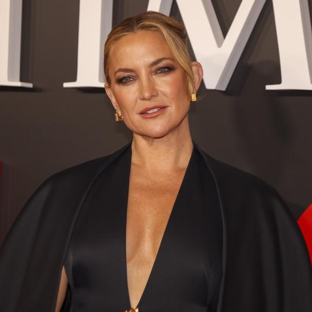 Kate Hudson trägt ein schwarzes Kleid vor einem Hintergrund mit roten und weißen Elementen.
