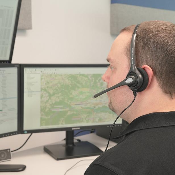 Ein Mann mit Headset sitzt vor mehreren Monitoren mit Karten- und Tabellendarstellungen.