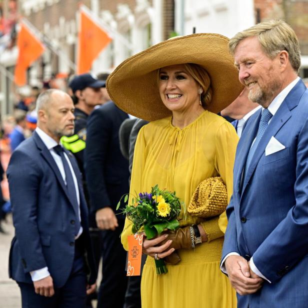 König Willem-Alexander und Königin Máxima lächeln inmitten einer Menschenmenge mit orangefarbenen Flaggen.