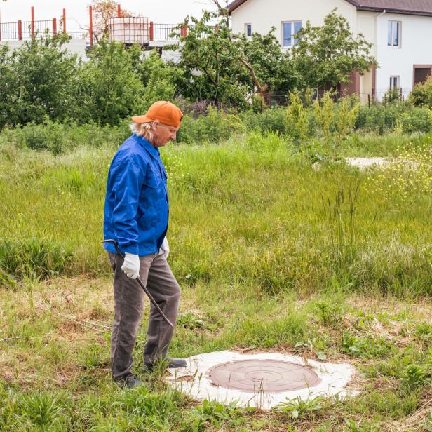Ein Handwerker  steht vor dem Kanaldeckel auf einer Liegenschaft 