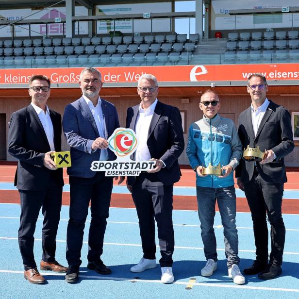 Fünf Männer stehen auf einer blauen Laufbahn und halten Schilder sowie goldene Kronen in den Händen.