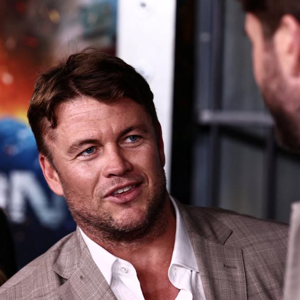 Luke Hemsworth mit Sakko spricht mit einer anderen Person.
