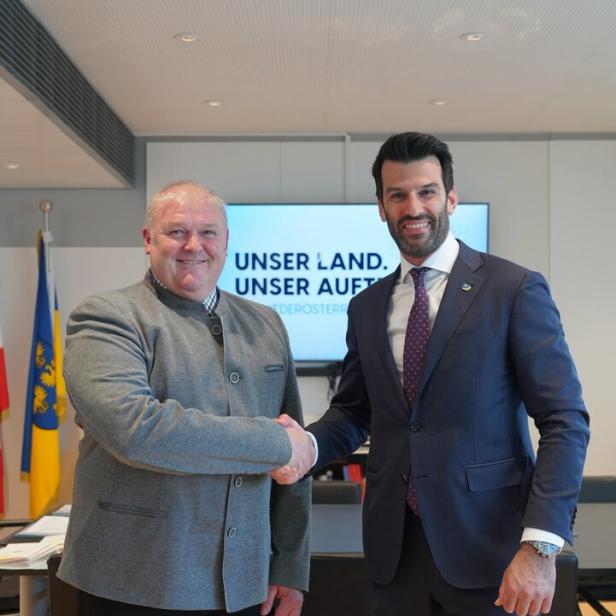 Zwei Männer schütteln sich vor einem Bildschirm mit der Aufschrift "Unser Land. Unser Auftrag.".