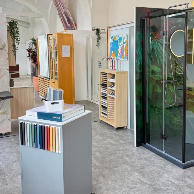 Moderne Badausstellung mit Waschtisch, Farbmusterbox und Duschkabine mit Papageienmotiv.
