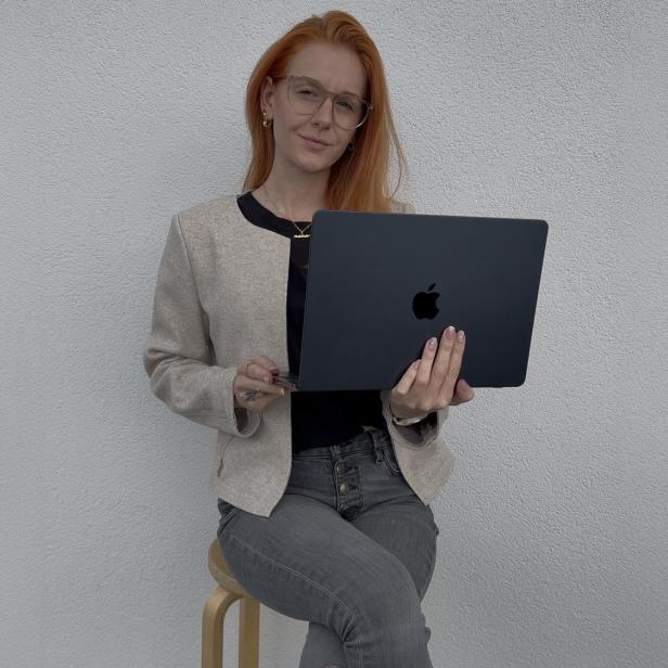 Eine Frau sitzt auf einem Hocker und hält ein Apple-Laptop in den Händen.