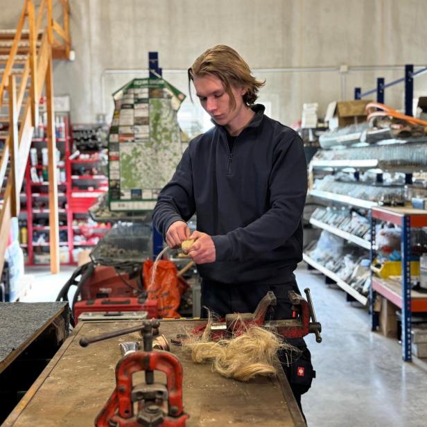 Ein junger Mann arbeitet an einer Werkbank in einer Werkstatt und hält Hanffasern in den Händen.