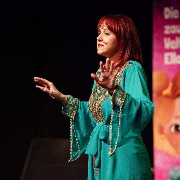 Eine Frau in einem türkisfarbenen Kleid spricht auf der Bühne.