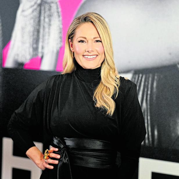 Helene Fischer lächelt in einem schwarzen Kleid mit Gürtel vor einem Hintergrund.