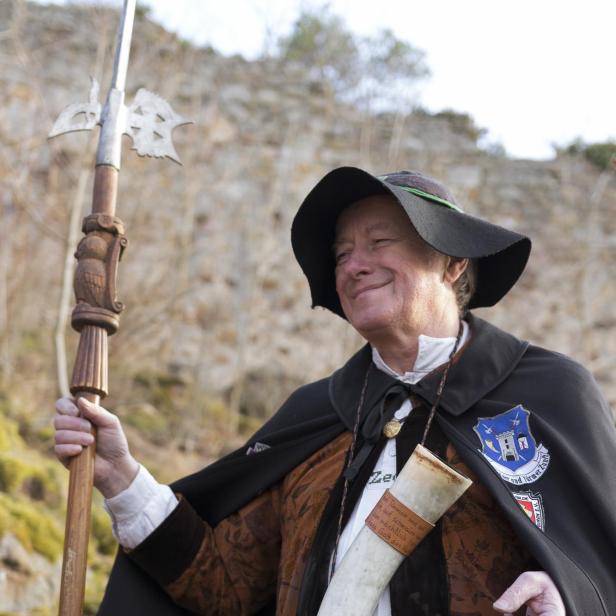 Ein Nachtwächter in traditioneller Kleidung mit Hellebarde, Horn und Laterne im Freien.