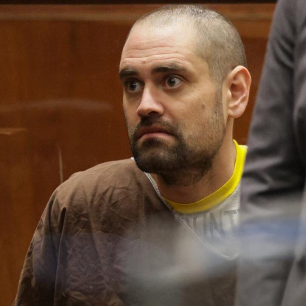 Nick Reiner mit kurzem Haar und Bart trägt braune Kleidung und sitzt mit ernstem Gesichtsausdruck in einem Raum mit Holzvertäfelung.