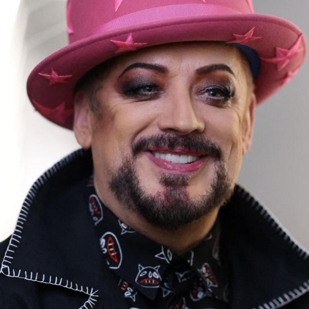Boy George lächelt mit pinkem Hut und auffälligem Make-up.