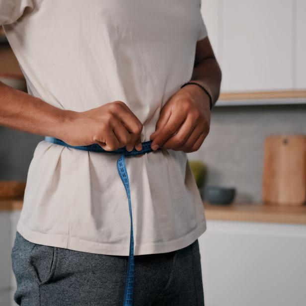 Unrecognizable sporty male sports man African guy measures waist with measuring tape check weight loss training workout sport dieting healthy nutrition control calories body muscle mass centimeters