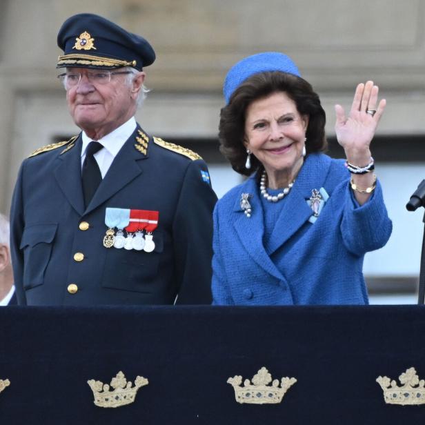 König Carl XVI. Gustaf und Königin Silvia winken von einem Balkon.