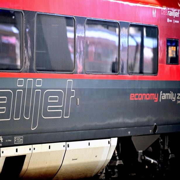Seitliche Ansicht eines roten Railjet-Zugwagens mit großen Fenstern und der Aufschrift „railjet“ sowie „economy family zone“.