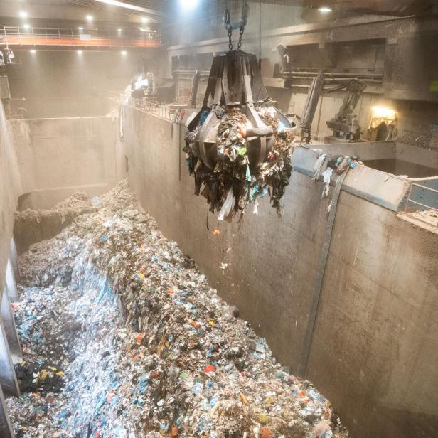 Eine Greifzange hievt Müll über einen riesigen Abfallbunker in einer Industrieanlage.