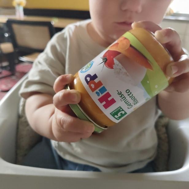 Ein Kleinkind hält ein Glas mit Hipp Gemüse Risotto Babynahrung in der Hand.