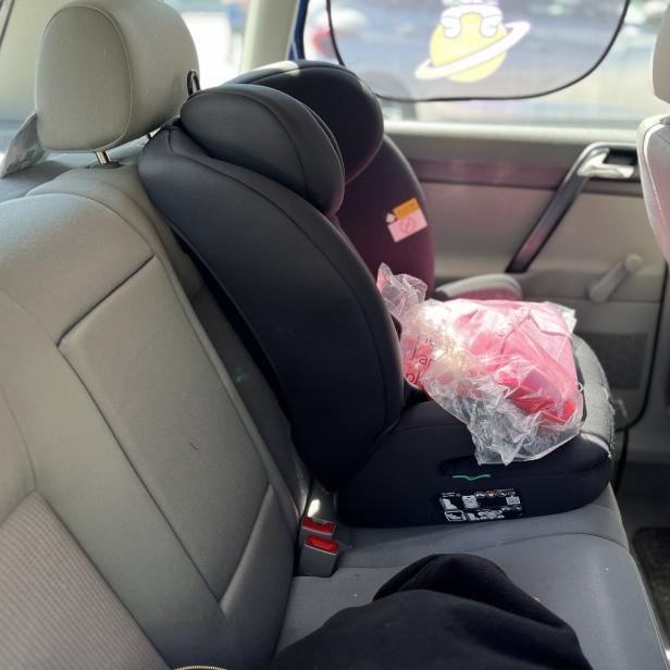 Kindersitz mit einer in Plastik verpackten Jacke auf dem Rücksitz eines Autos.