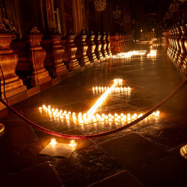 Viele kleine Kerzen bilden ein großes Ankersymbol auf dem Boden eines festlich beleuchteten Kirchenraums.