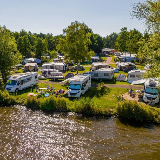 Ein Campingplatz am Wasser mit Wohnwagen, Zelten und Badegästen unter blauem Himmel.