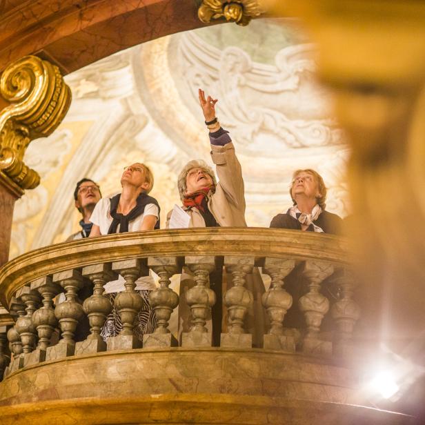 Besucherinnen und Besucher bestaunen gemeinsam die kunstvoll bemalte Decke einer prunkvollen Wiener Kirche während der Langen Nacht der Kirchen.
