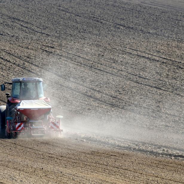 Ein Traktor bearbeitet ein großes Feld, Staub wirbelt auf.