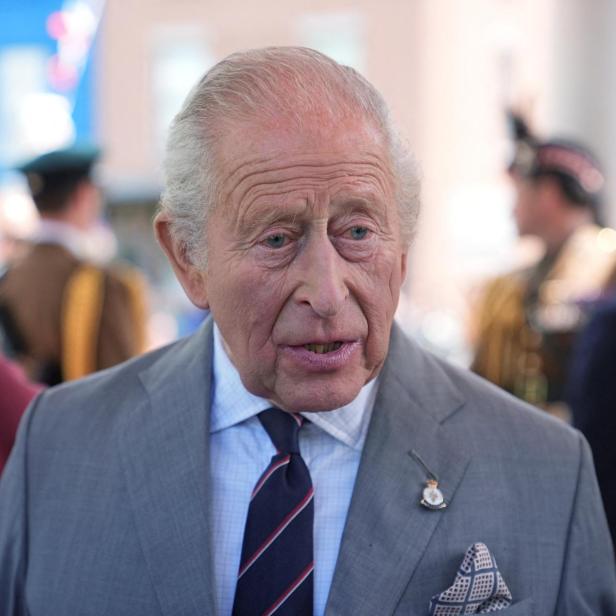 König Charles III. im grauen Anzug mit gestreifter Krawatte und Einstecktuch.