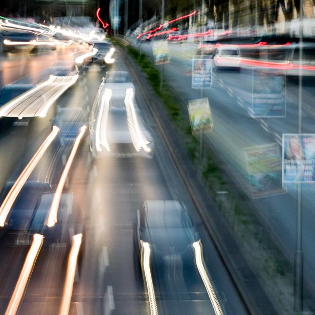 Mehrspurige Stadtautobahn mit vorbeifahrenden Autos und verschwommenen Lichtspuren bei Nacht.