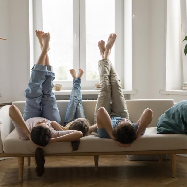Zwei Menschen liegen lachend kopfüber auf einem Sofa, halten Händchen und strecken die Beine in bunten Socken nach oben.