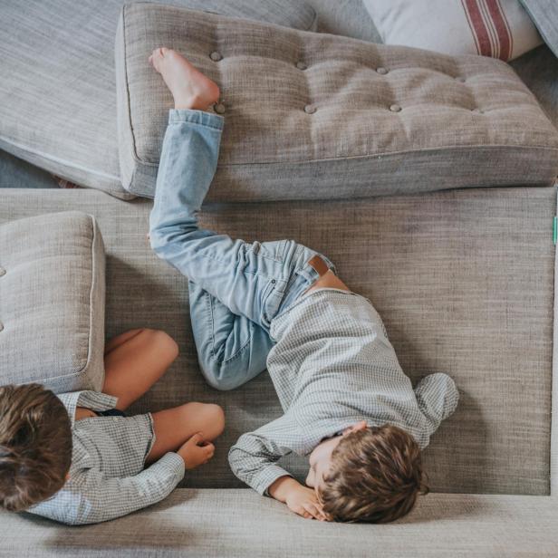 Zwei Jungen liegen entspannt auf einem grauen, modularen Sofa mit Knopfheftung