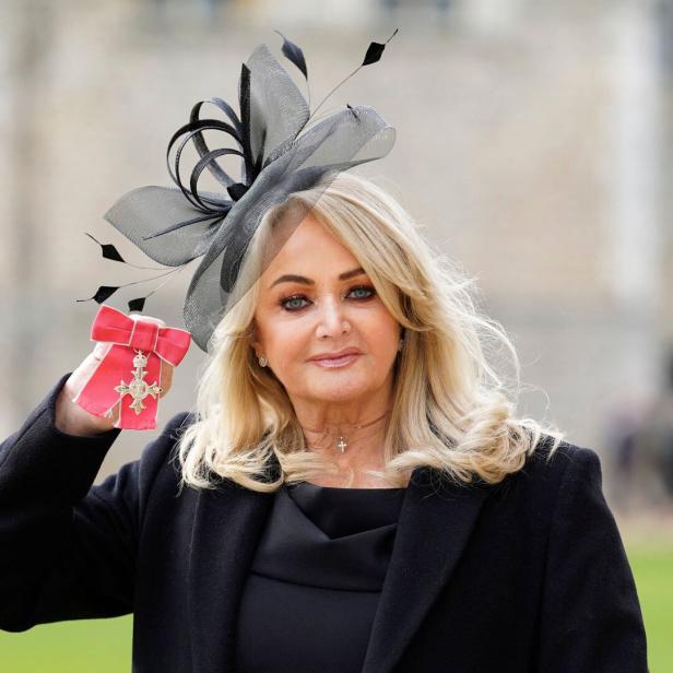 Eine blonde Bonnie Tyler mit Hut hält eine Auszeichnung mit roter Schleife in der Hand.