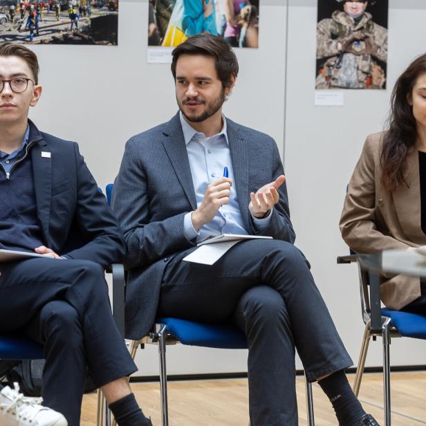 Drei junge Erwachsene in Businesskleidung sitzen nebeneinander und diskutieren in einem modernen Raum.