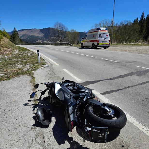 Ein Motorrad liegt umgestürzt am Straßenrand, daneben ein beschädigter Helm und ein Rettungswagen steht weiter vorne.