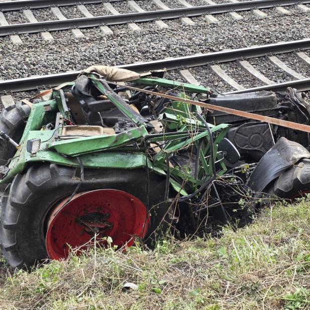 Ein zerstörter, grüner Traktor liegt neben Bahngleisen im Gras.