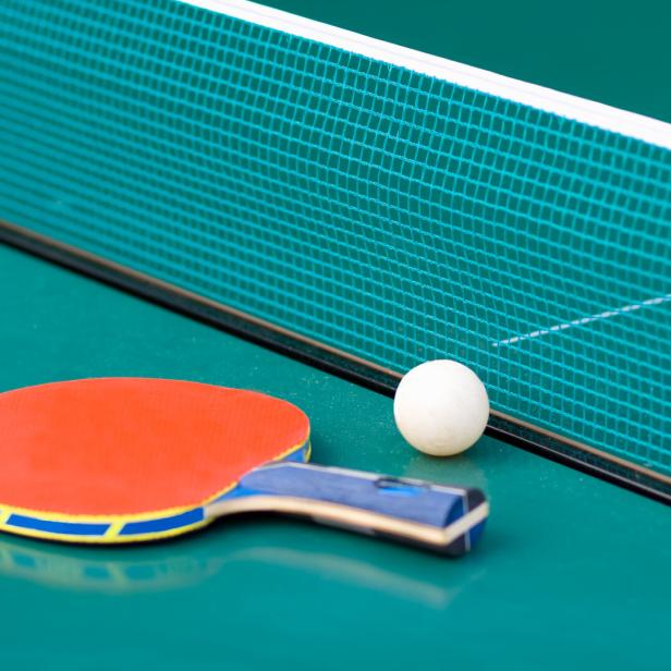 Tischtennisschläger und Ball liegen vor dem Netz auf grünem Tisch.