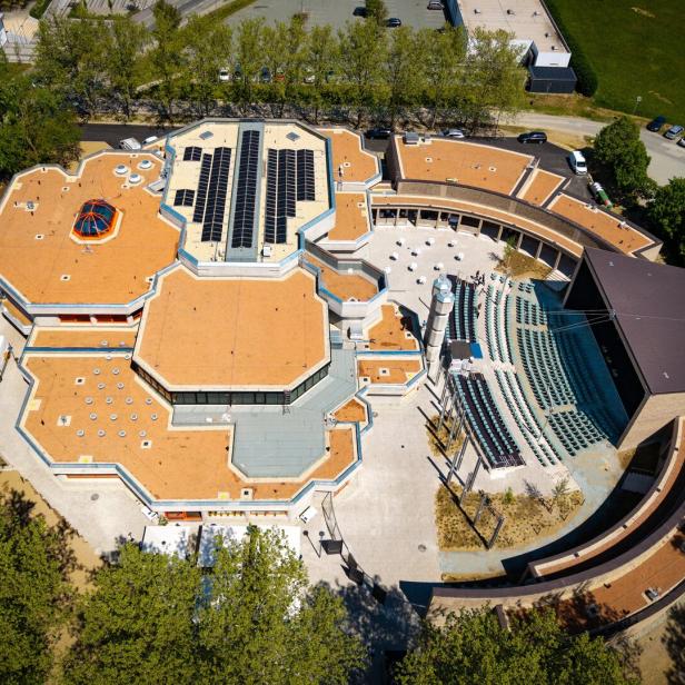 Luftaufnahme eines Gebäudes mit orangefarbenem Dach, Solarmodulen und einem Amphitheater.