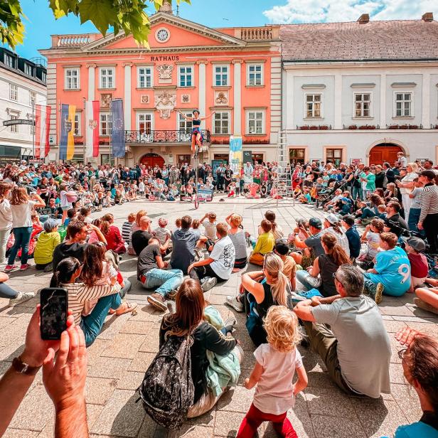 Straßenkünstler tritt vor großem Publikum auf dem Hauptplatz vor dem Rathaus in Wiener Neustadt auf.