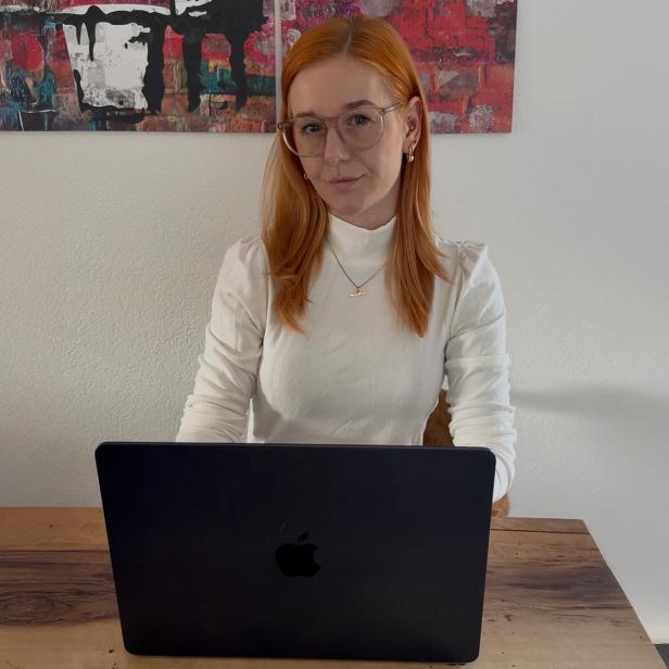 Eine rothaarige Frau in einem weißen Langshirt vor einem schwarzen Laptop 