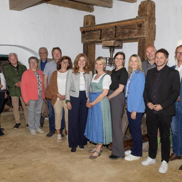 Mehrere Menschen stehen lächelnd vor einer historischen Weinpresse im Presshaus.