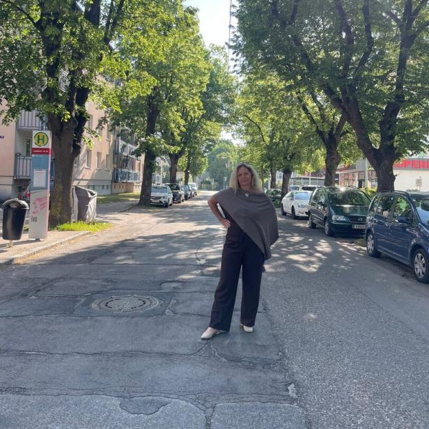 Eine Frau steht auf einer von Bäumen gesäumten Straße, umgeben von geparkten Autos und Sonnenschein.