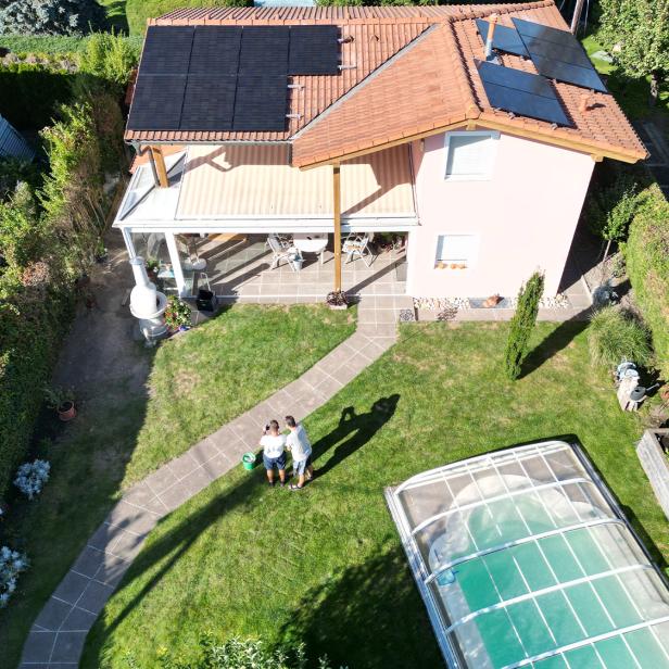 Haus mit Photovoltaikanlage auf dem Dach, Garten und überdachtem Pool bei Sonnenschein.