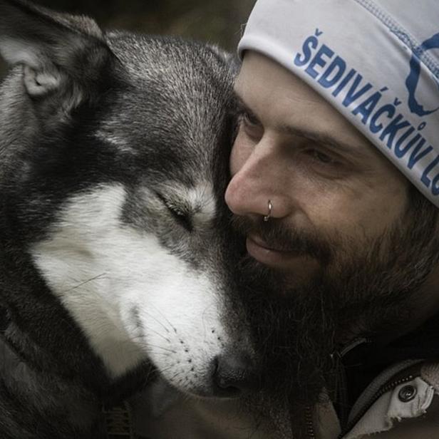 Ein Mann mit Mütze kuschelt eng mit einem Husky, beide wirken entspannt und verbunden.