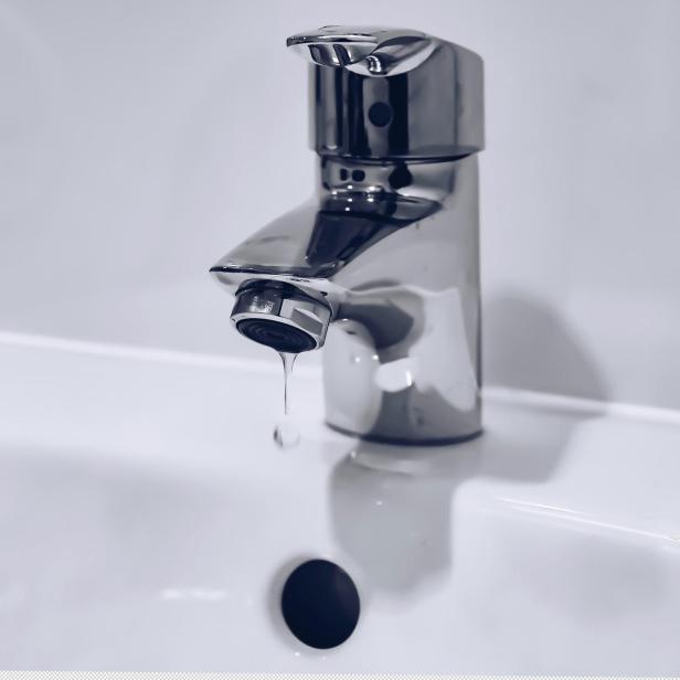 Einzelner Wassertropfen tropft aus einem Wasserhahn in ein weißes Waschbecken.