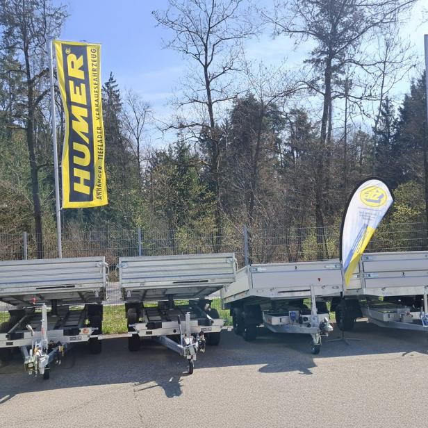 Mehrere PKW-Anhänger verschiedener Modelle auf einem Ausstellungsplatz mit HUMER-Fahnen.