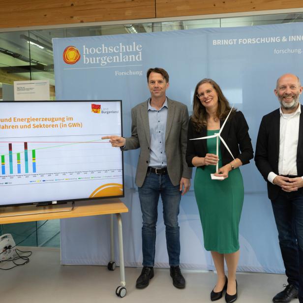 Drei Personen stehen vor einem Diagramm zum Energieverbrauch im Burgenland, eine Frau hält ein Windradmodell.
