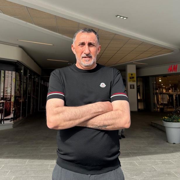Ein Mann mit verschränkten Armen steht vor einem Einkaufszentrum mit H&M-Eingang im Hintergrund.